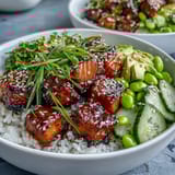 A close-up of a vibrant Salmon Rice Bowl reveals creamy avocado and toasted sesame seeds over warm rice and baked marinated salmon.