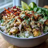Close-up view of a Peanut Chicken Protein Bowl showing creamy peanut sauce drizzled over fresh cilantro and chopped peanuts.
