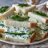 Kentucky Derby Benedictine tea sandwiches with cucumber and cream cheese on white bread, garnished with fresh dill, served on a floral platter.