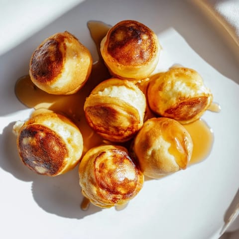 Mini pancake bites, perfectly round and puffed, with visible fruit pieces ready for brunch.