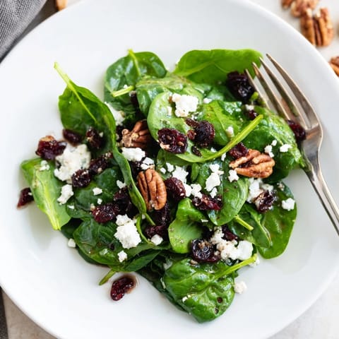 A vibrant, ready-to-eat spinach goat cheese salad served as a light lunch, topped with extra candied pecans and cranberries for crunch.