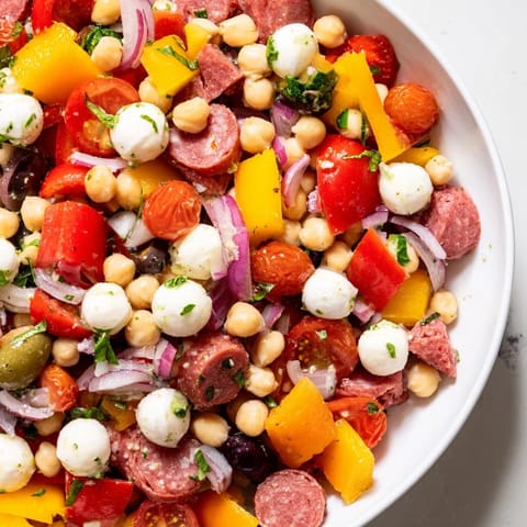 A close-up of Crunchy Antipasto Chopped Salad with chickpeas, salami, and mozzarella glistening in Italian dressing.
