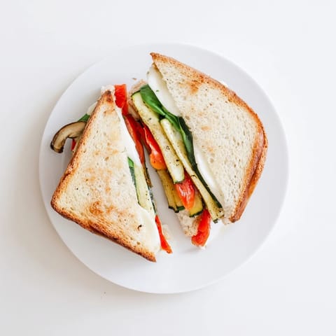 A close-up of a crispy Roasted Veggie Caprese Grilled Cheese, revealing melted mozzarella and juicy tomatoes between golden bread slices.  