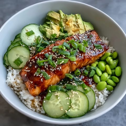 A vibrant bowl of honey sriracha glazed salmon over jasmine rice with fresh cucumber, edamame, and creamy avocado slices.  