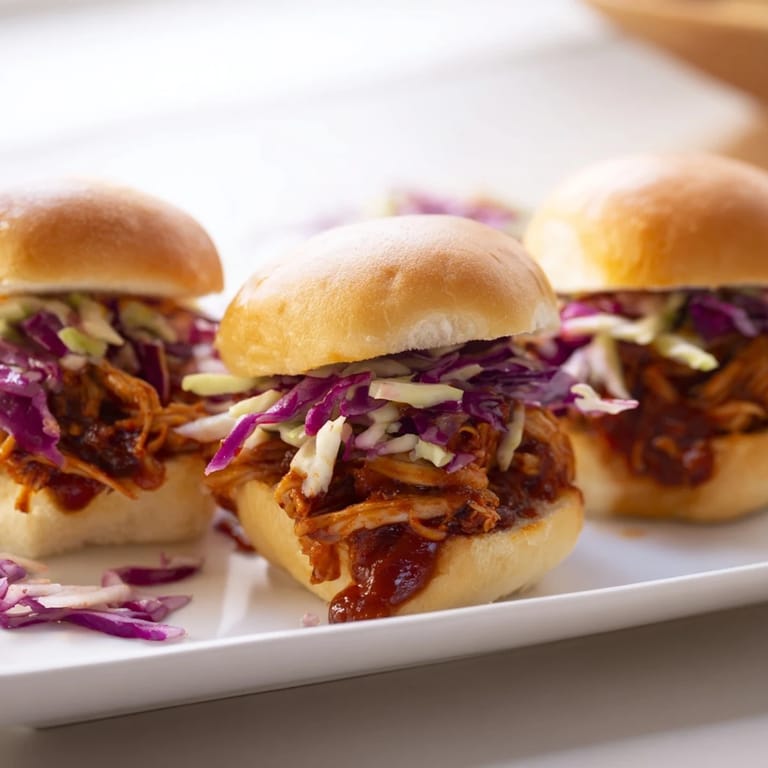 Juicy pulled BBQ chicken filling soft slider buns with a colorful, tangy slaw topping on a wooden board.