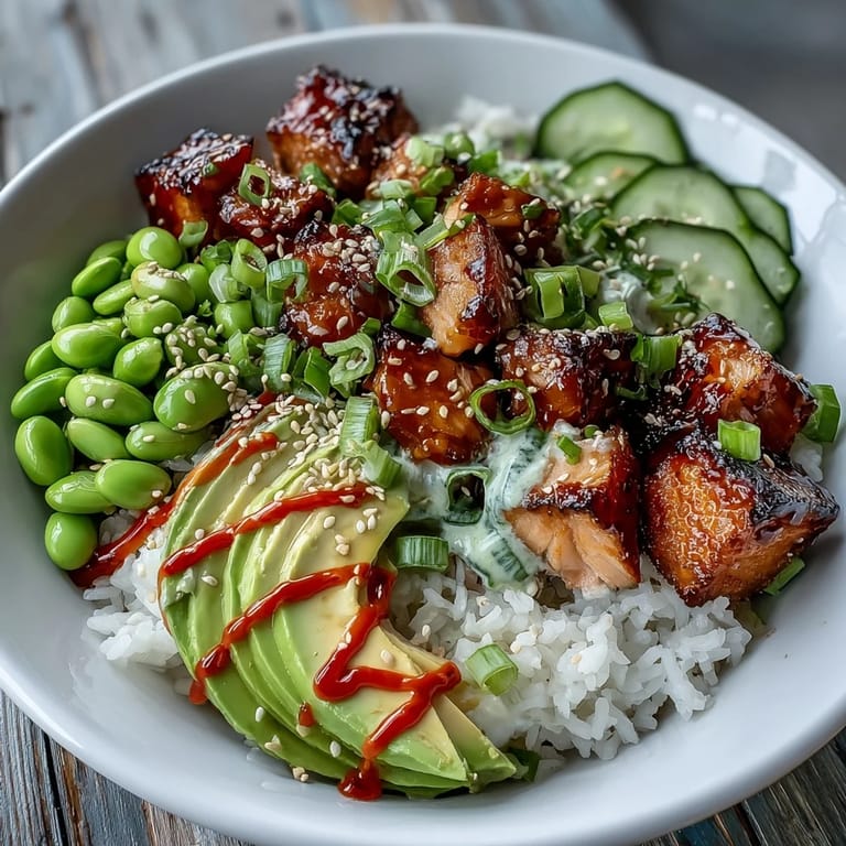 A deconstructed Salmon Rice Bowl with spicy sriracha mayo drizzle over salmon, cucumber, and avocado on jasmine rice.