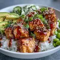 Golden baked salmon cubes sit on fluffy jasmine rice with bright green edamame and crisp cucumber slices in this Salmon Rice Bowl, drizzled with creamy sriracha mayo.