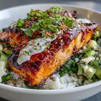 Flaky baked salmon topped with creamy bang bang sauce rests on rice with a crisp cucumber-edamame salsa.
