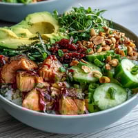 A vibrant Avocado Salmon Bowl with avocado slices, tamari-glazed salmon, and peanuts over steamed rice, finished with chili oil and wasabi.